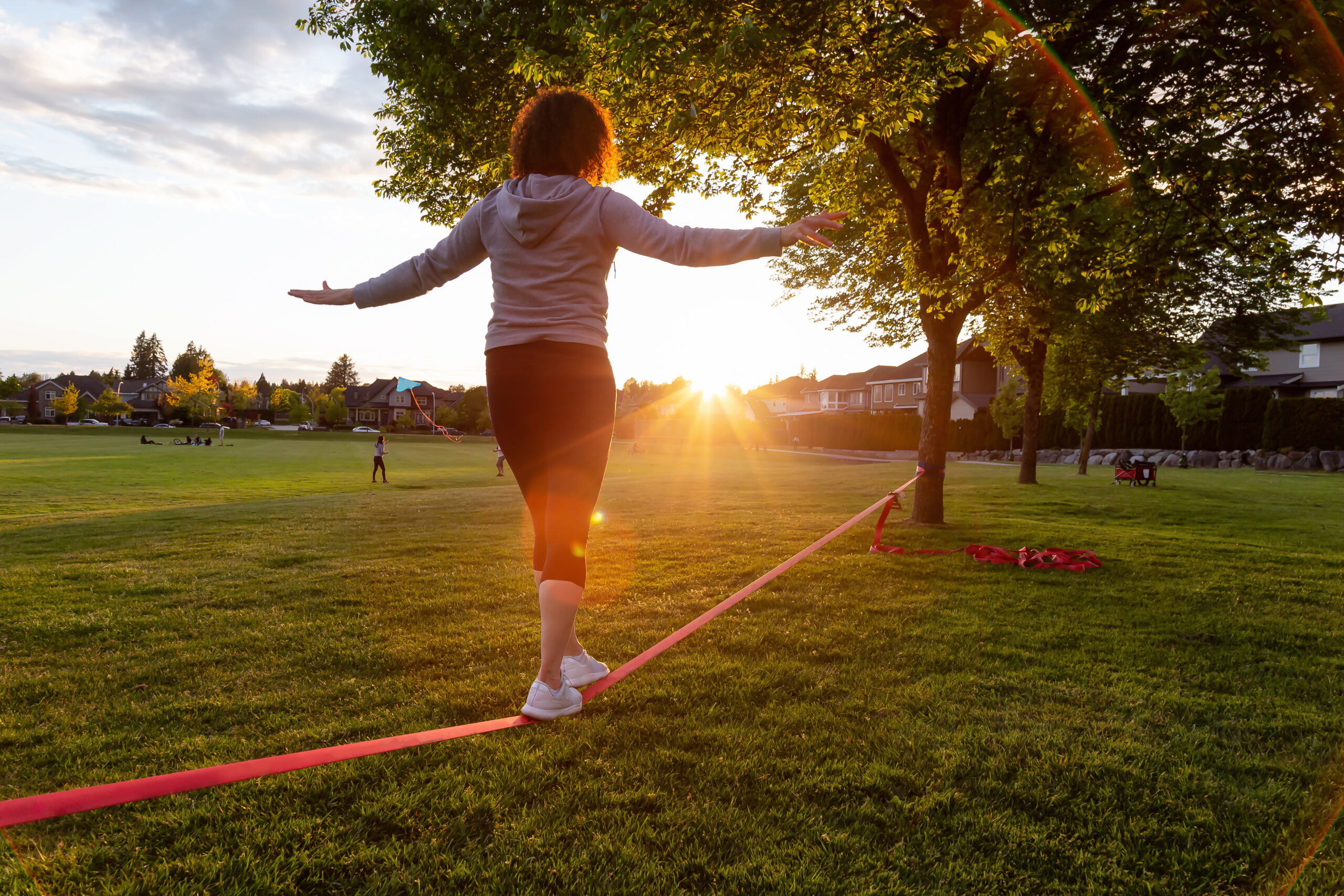 Girl walking on a Slackline in a park during a sunny sunset.