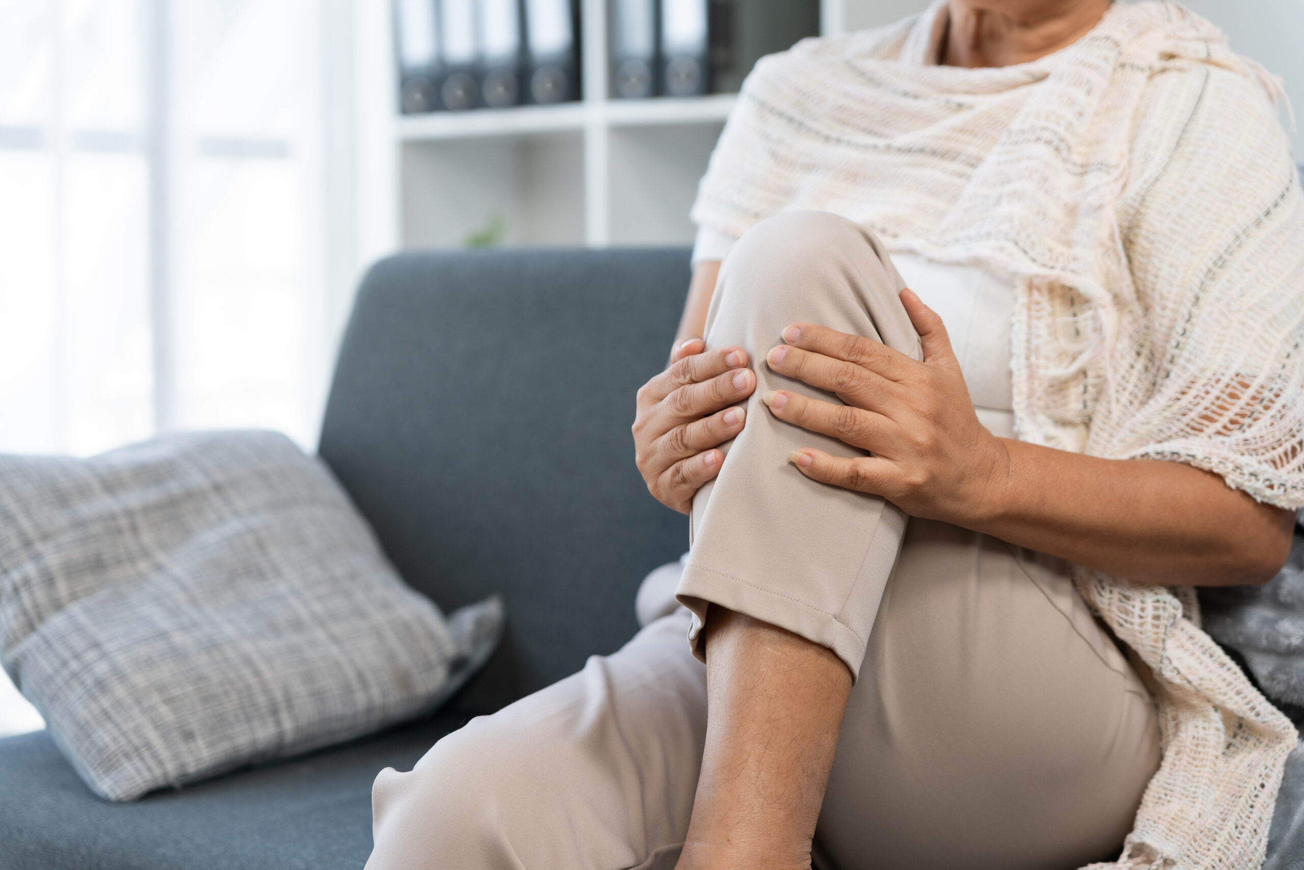 Elderly woman experiencing knee pain, holding leg