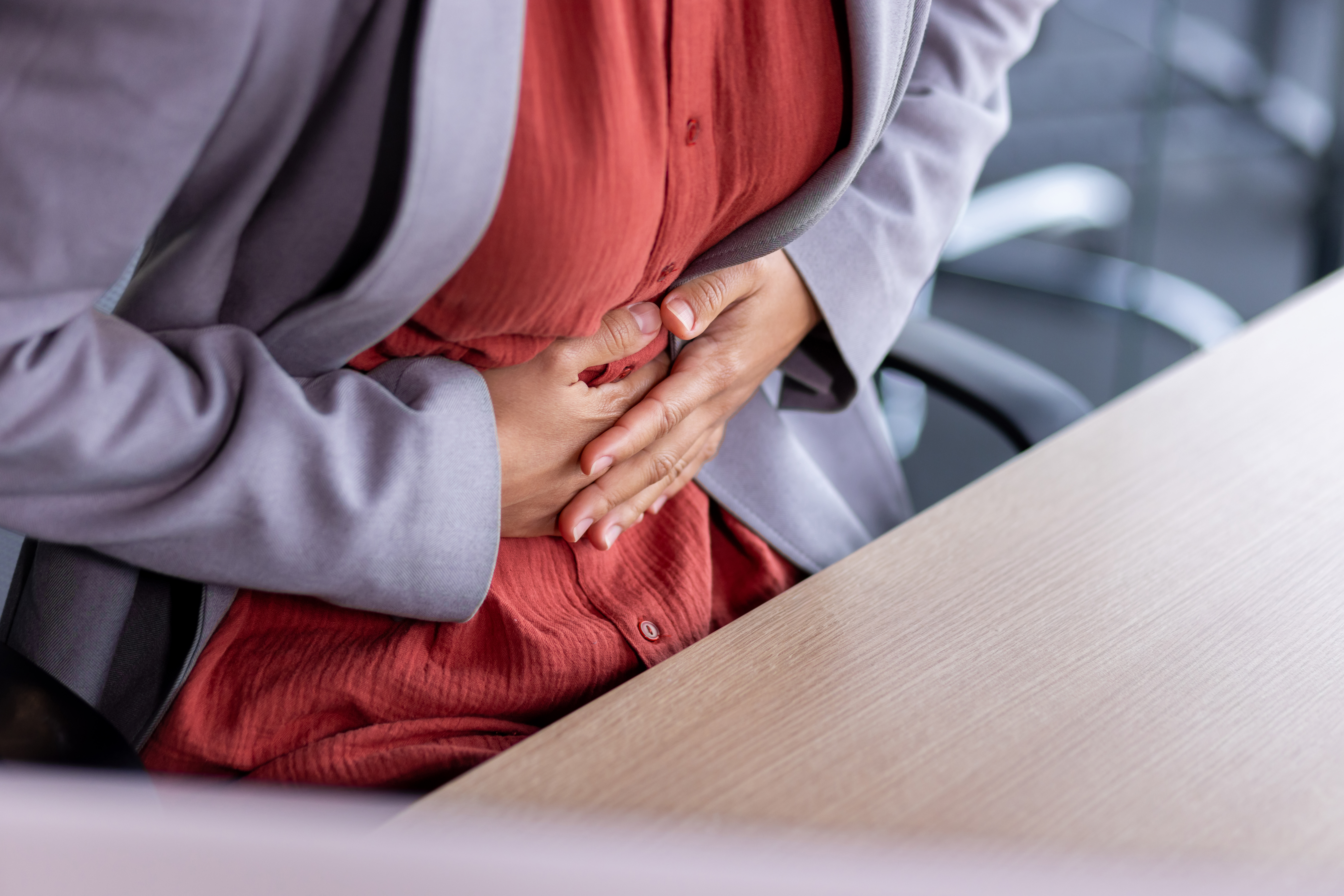 Stomach ache, sick business woman holding hands on stomach close up, female worker at workplace working at table with laptop inside office